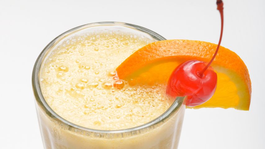 Koktajl mleczny z owocami w szklance na białym tle. Na krawędzi szklanki kawałek pomarańczy i czereśnia.